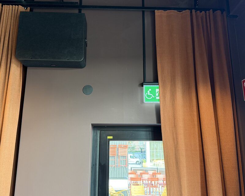 Högtalare diskret monterad högt på vägg i restaurang